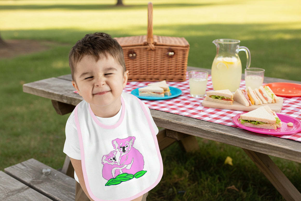 toddler wearing a bib with a koala design on a pink background