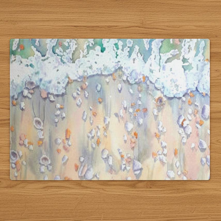 A rectangular placemat in watercolor art print featuring an abstract painting of ocean waves washing onto a sandy beach, with shells and small orange accents.