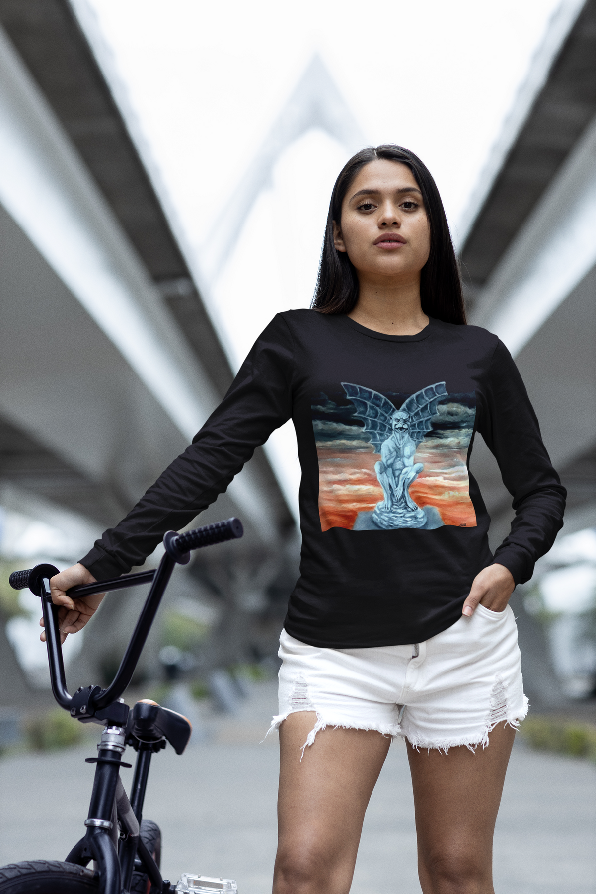 Girl wearing a black long-sleeve shirt with a colorful Gargoyle design, standing next to a bicycle in an urban setting.