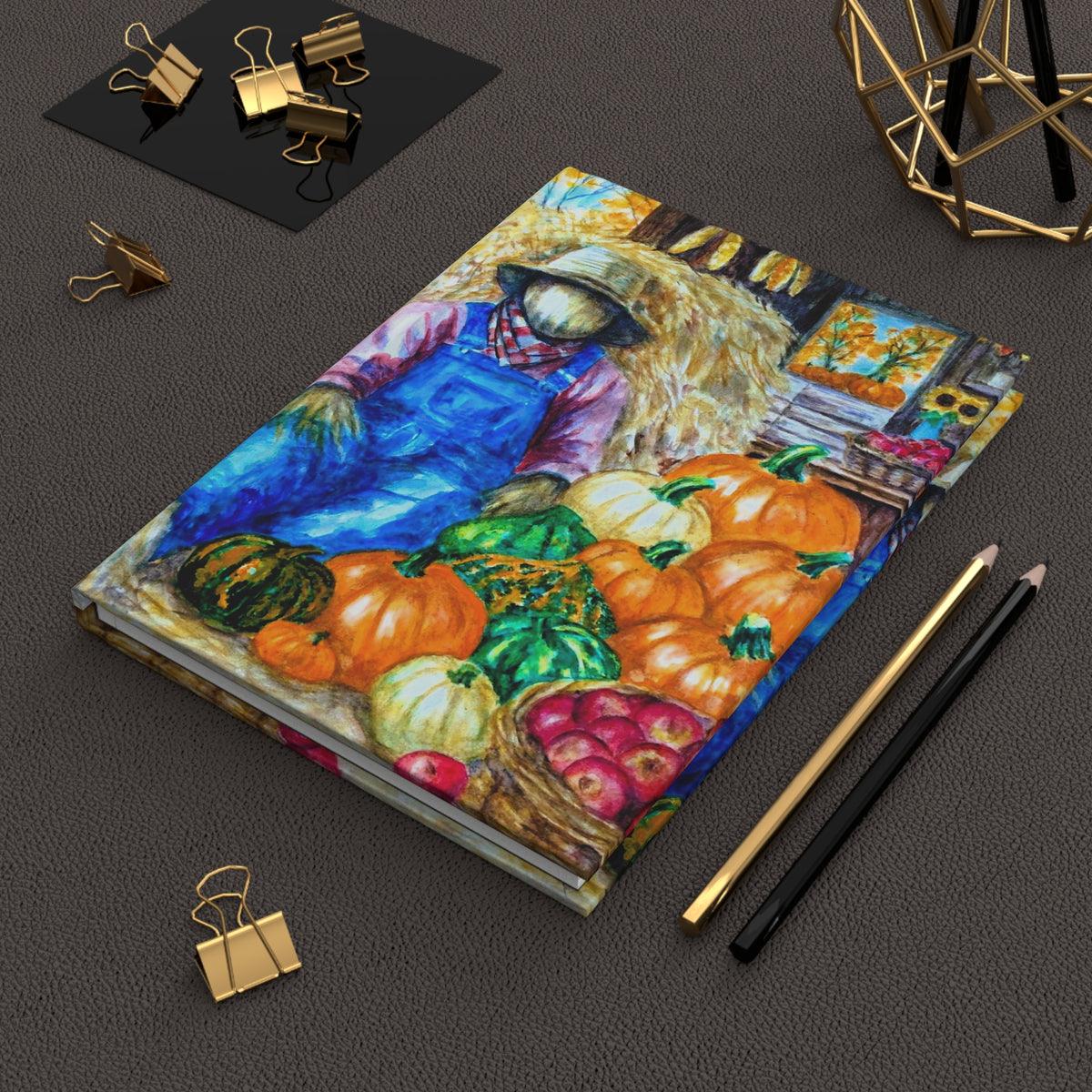 A hardcover notebook with a colorful painted illustration of a scarecrow and pumpkins and apples