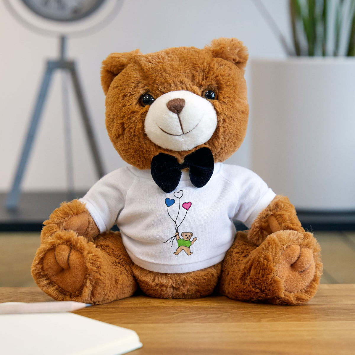 Brown teddy bear wearing a white tee shirt with a little brown bear illustration in a tee holding a group of balloons