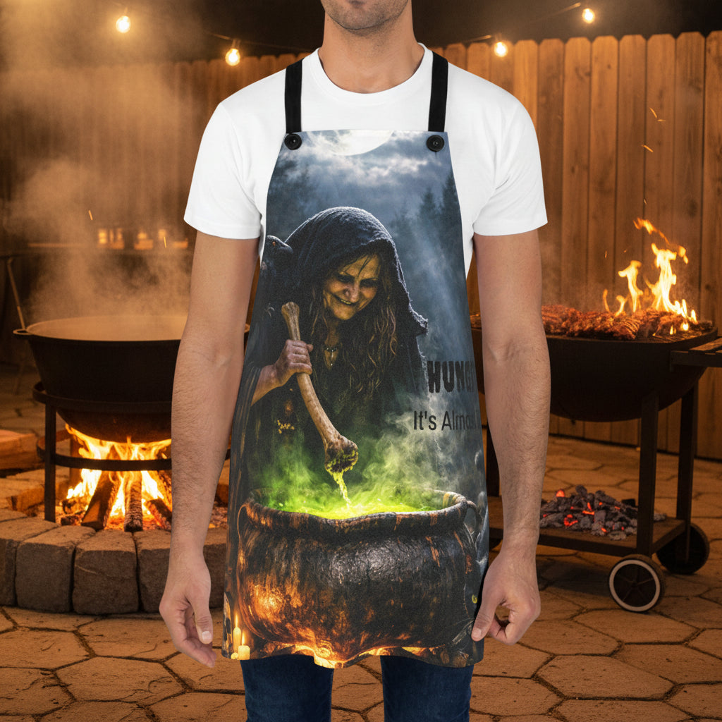 Halloween spooky black apron featuring a graphic print of a witch stirring a glowing cauldron with the text , Hungry? It's almost ready.