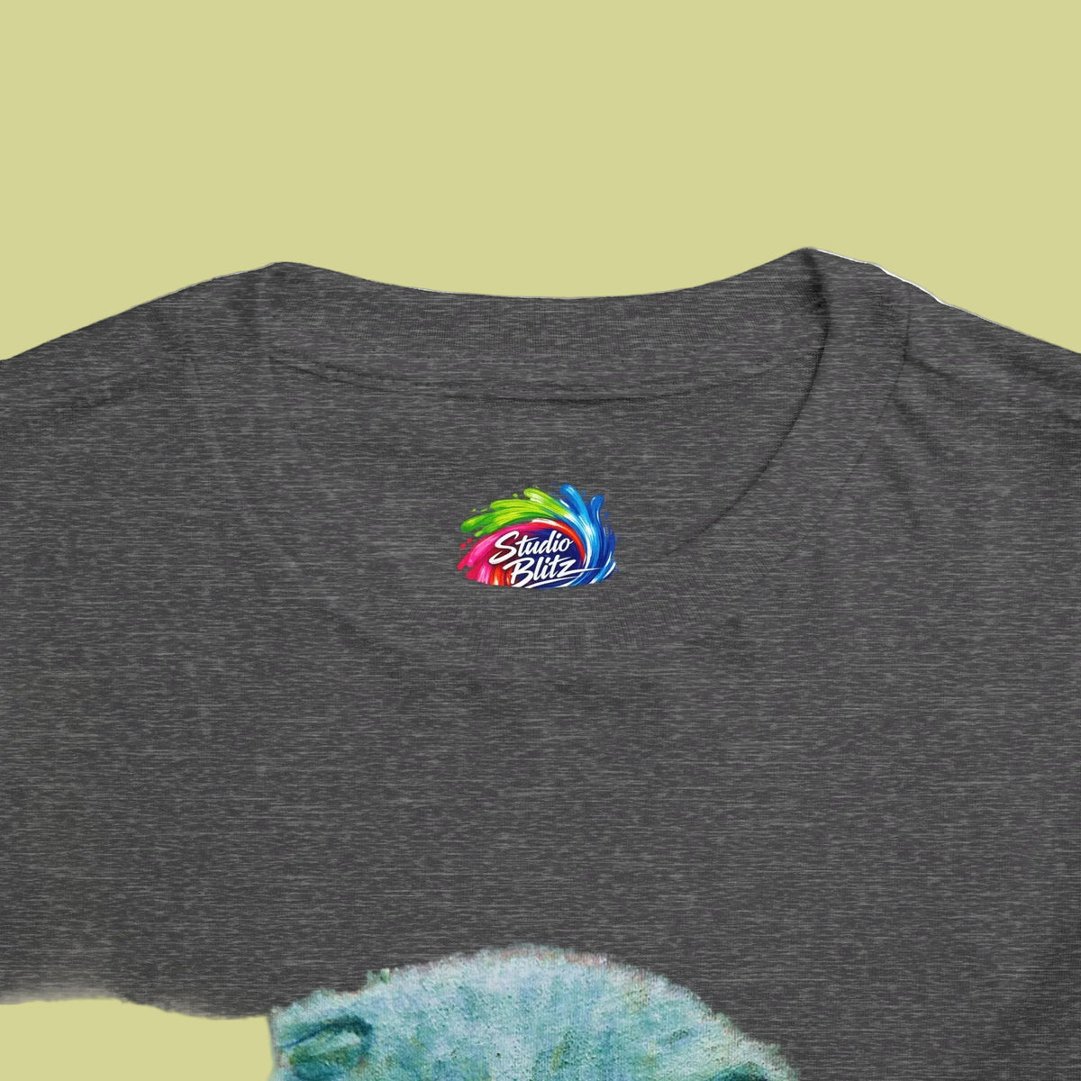 Close-up of a dark heather gray t-shirt featuring a colorful 'Studio Blitz' logo printed on the chest, with a blue textured graphic partially visible at the bottom.