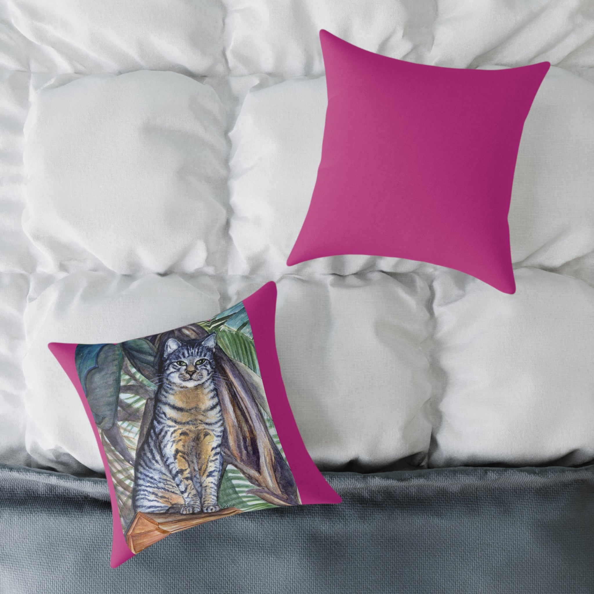 Two pillows on a bed, one with a cat illustration and the other solid pink.