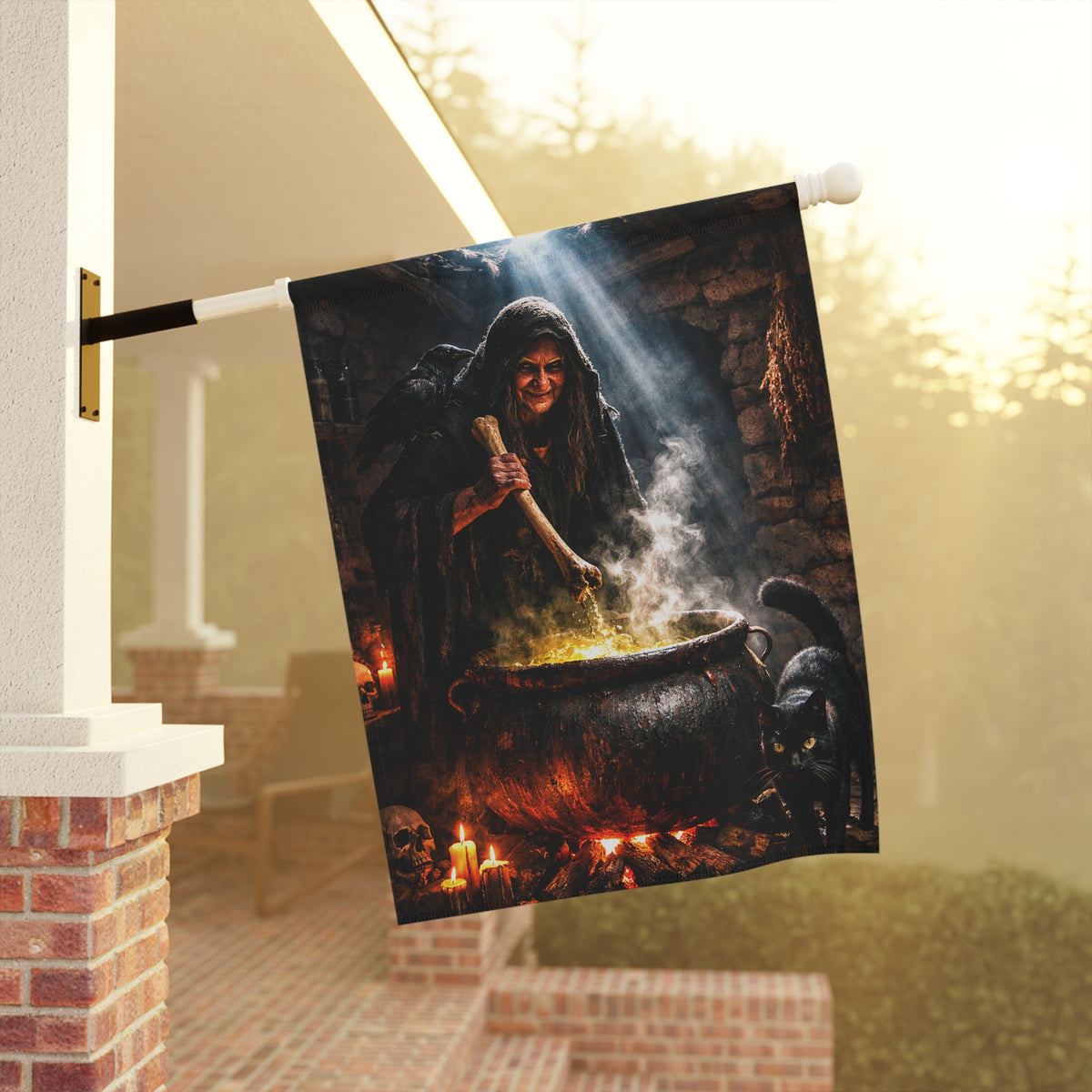A Spooky Halloween garden flag features a dramatic illustration of a witch in a dark cloak stirring a large cauldron with glowing yellow-orange fire, with a black cat and smoke in the scene.