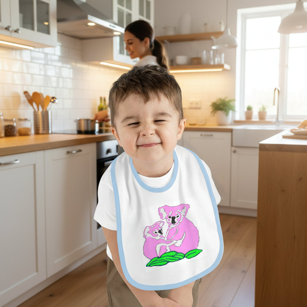 Child wearing a bib with a pink koala design on a white background and blue trim
