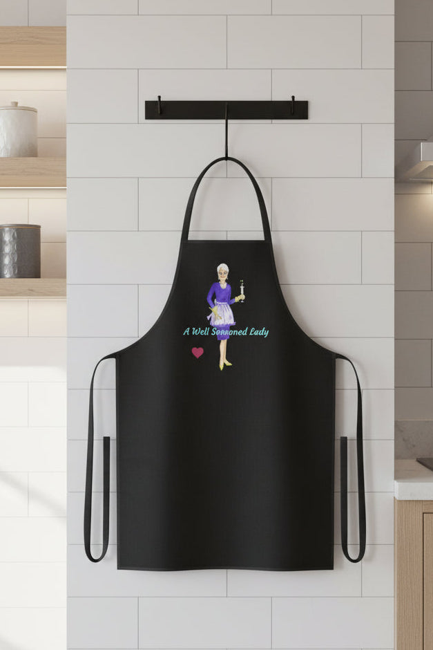 Black apron with an illustration of an elegant woman in an apron, spoon and a flute of champagne as 'A Well Seasoned Lady'
