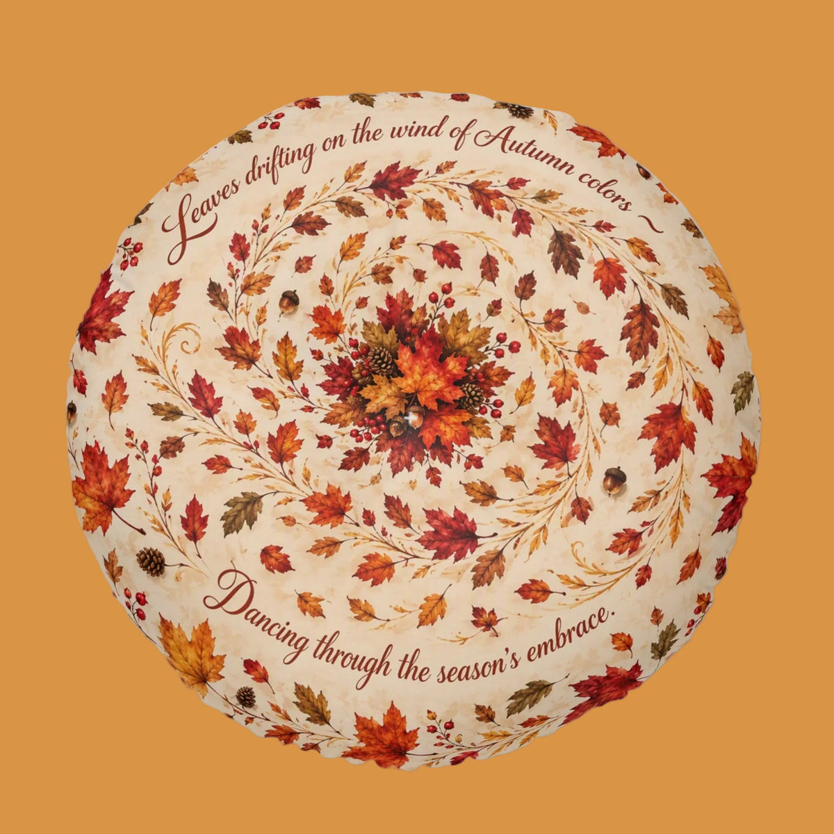 A round decorative throw pillow featuring an autumn-themed design with a cream background, a circular wreath of red, orange, and brown leaves, and cursive text that reads 'Leaves drifting on the wind of Autumn color' and 'Dancing through the season's embrace.'.