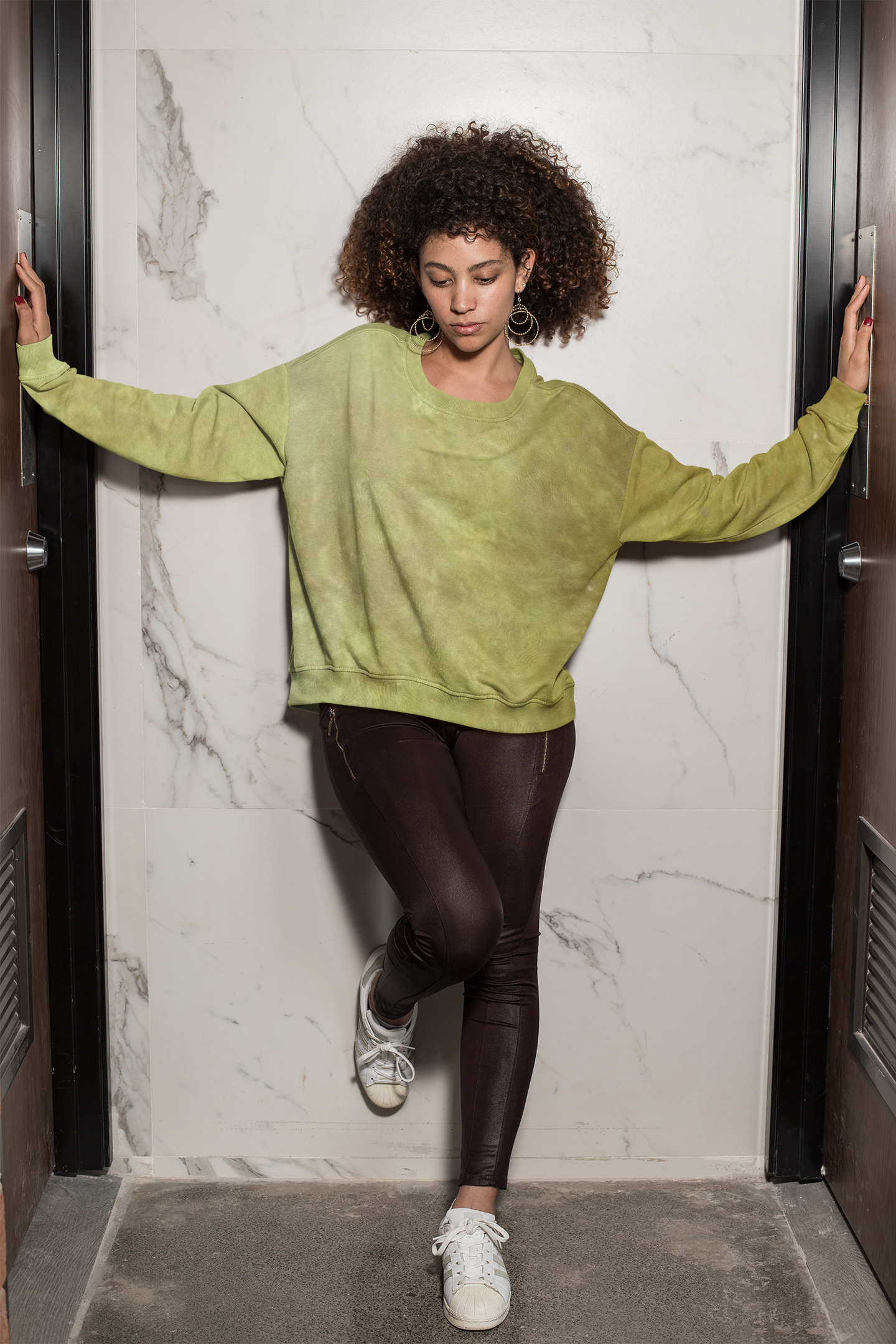 Woman wearing a greenish sweater and dark leggings standing in a doorway.