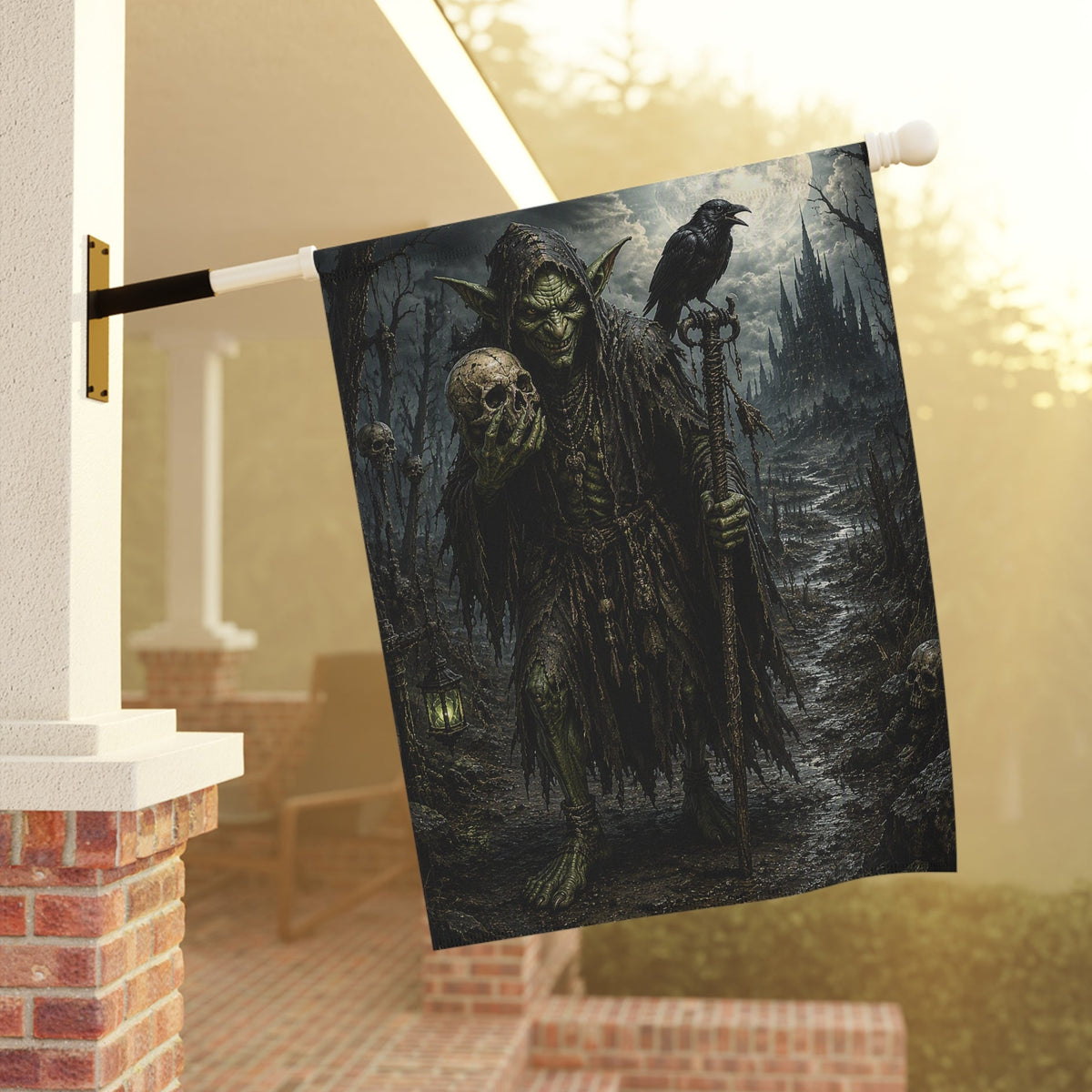 A Halloween-themed decorative garden flag. The flag features a dark, gothic illustration of a green-skinned goblin holding a skull and staff, with a raven perched on his shoulder, set against a misty forest background.