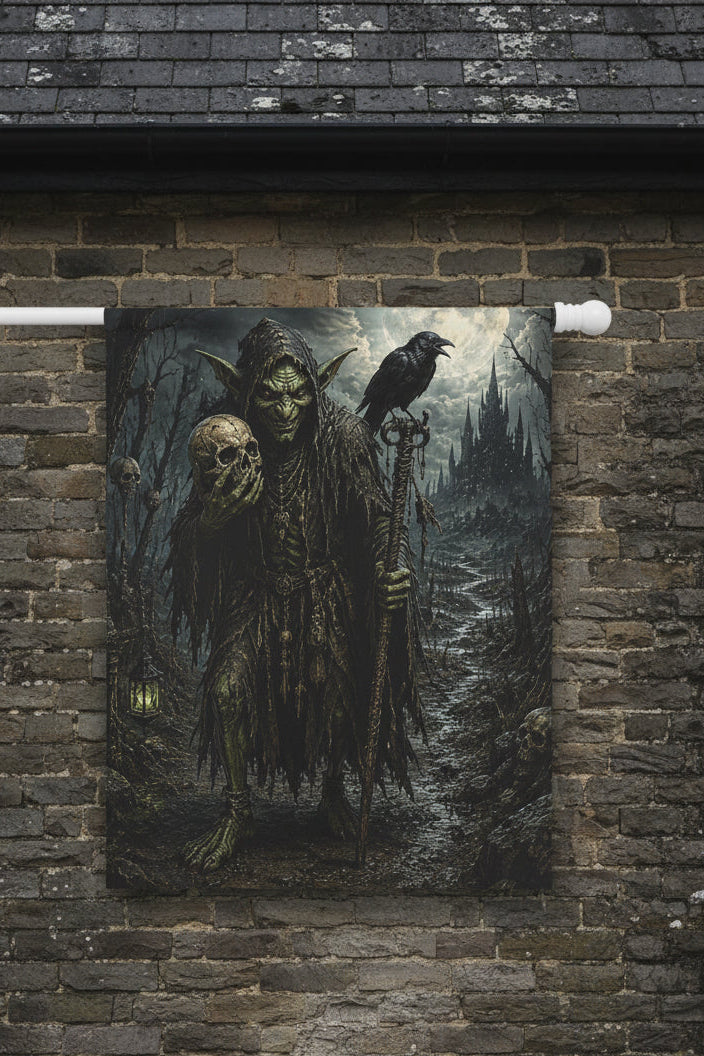 A vertical wall flag from a white rod, featuring a dark fantasy illustration of a green-skinned goblin-like figure in tattered robes, holding a skull and staff, with a raven perched on his shoulder and a ruined castle in the misty background.