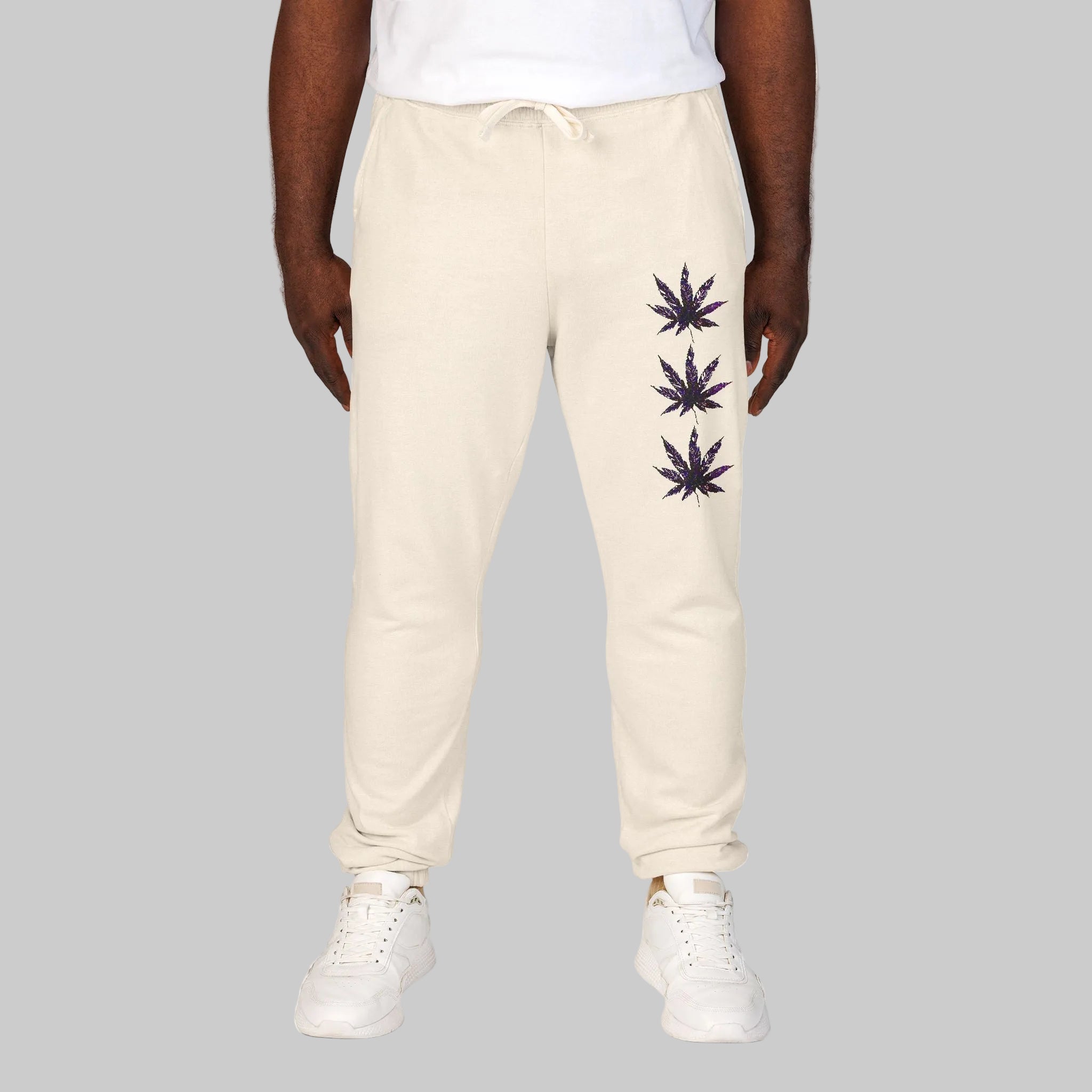 Ivory colored sweatpants with three  cannabis leaf graphics printed vertically on the left leg making you chi statement