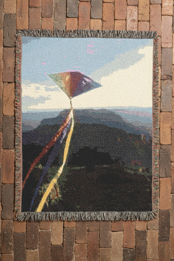 Woven blanket featuring a colorful kite against a mountainous landscape.