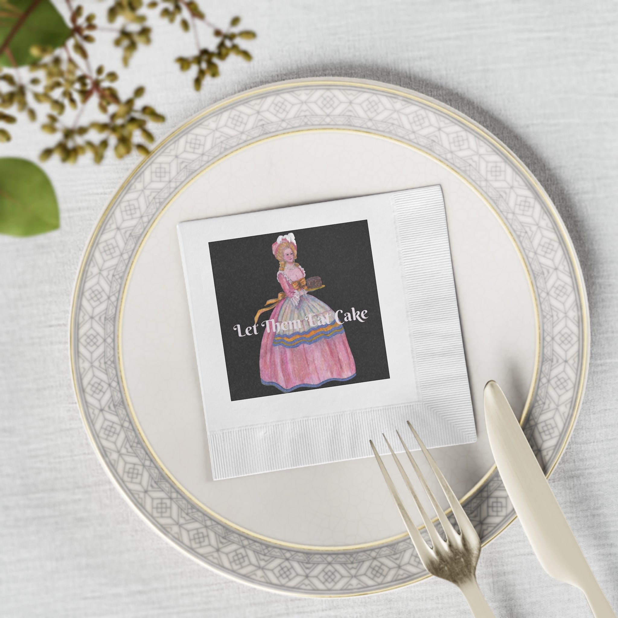 Place setting with a decorative plate, napkin, and cutlery on a light gray surface.