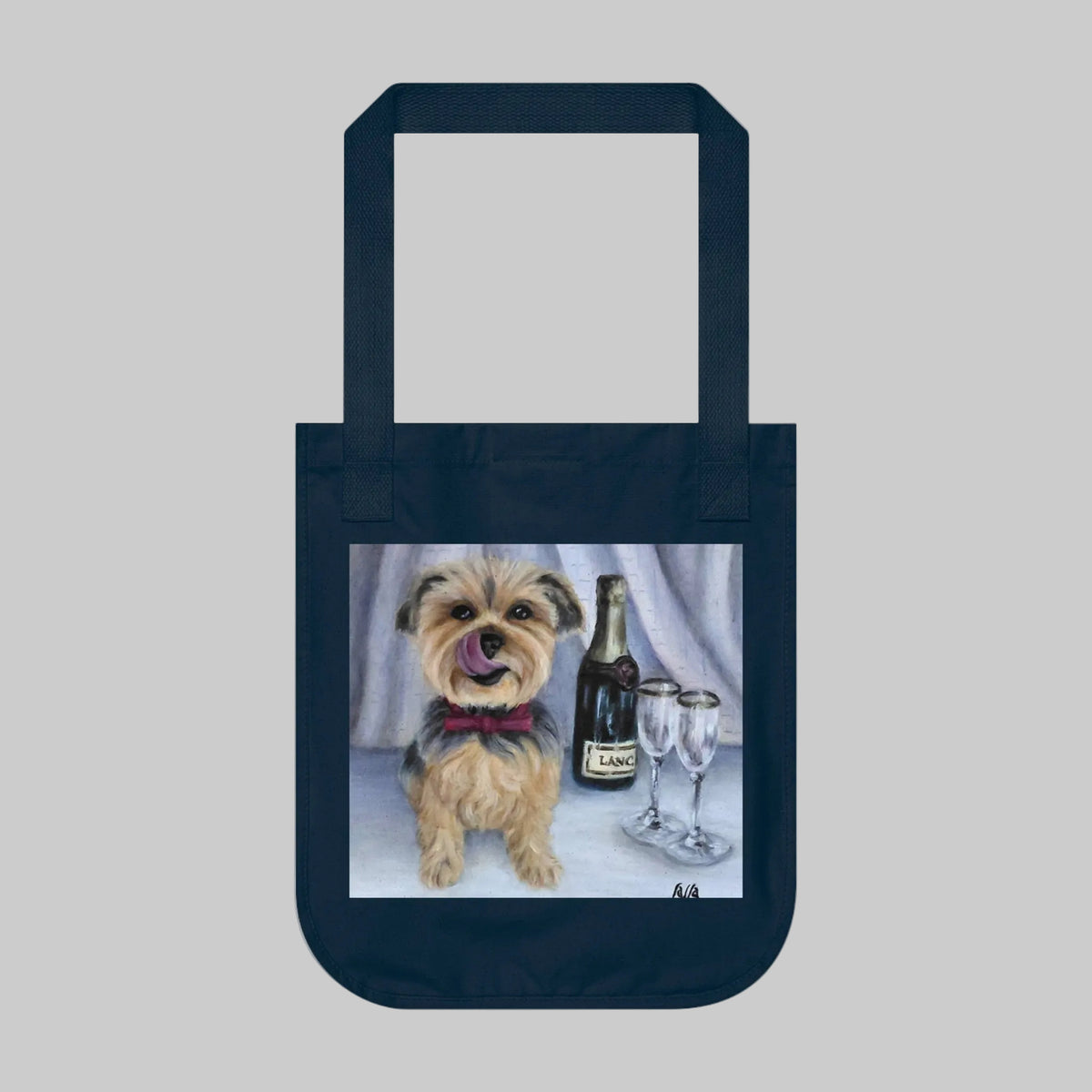 A dark navy blue canvas tote bag with a printed illustration of a small tan and grey dog wearing a red bow tie, sitting next to a wine bottle and two wine glasses.
