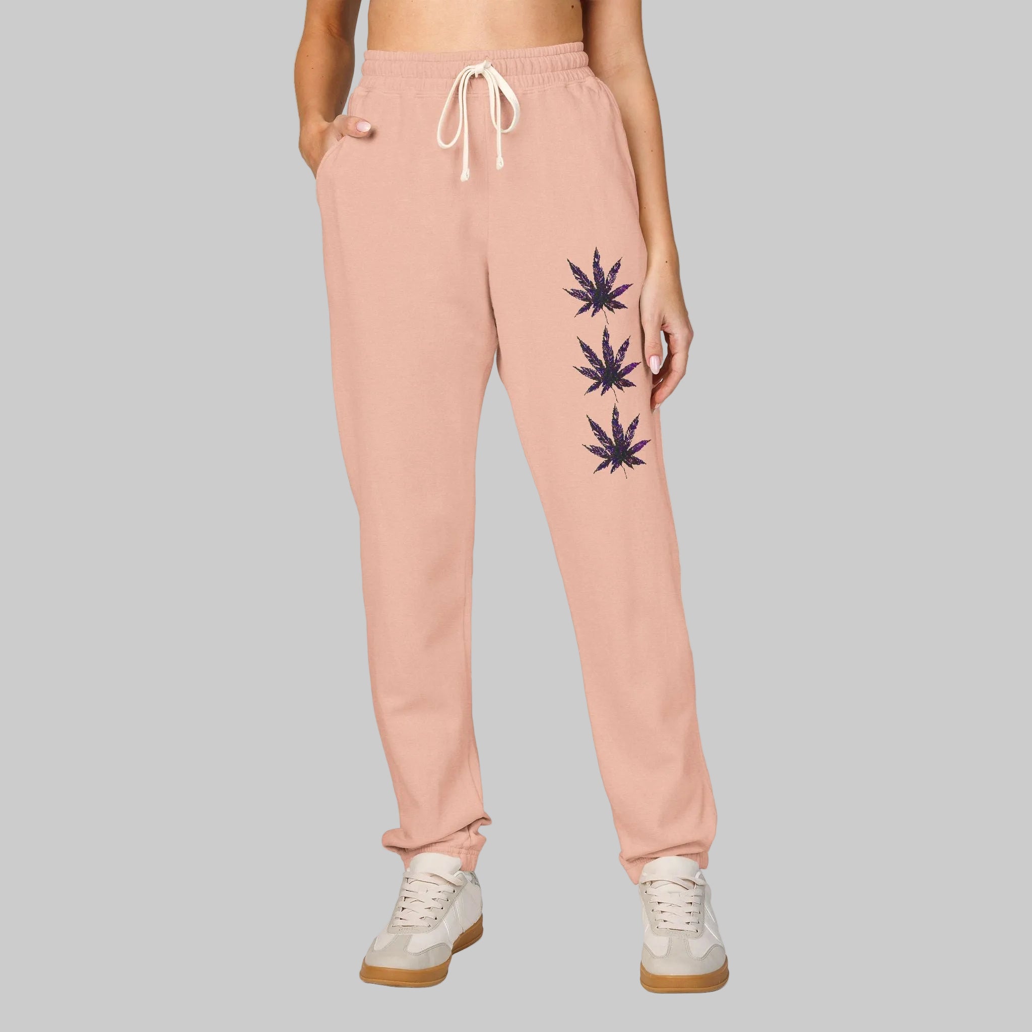 Peachy colored sweatpants with a white drawstring and three cannabis leaf graphics printed vertically on the left leg