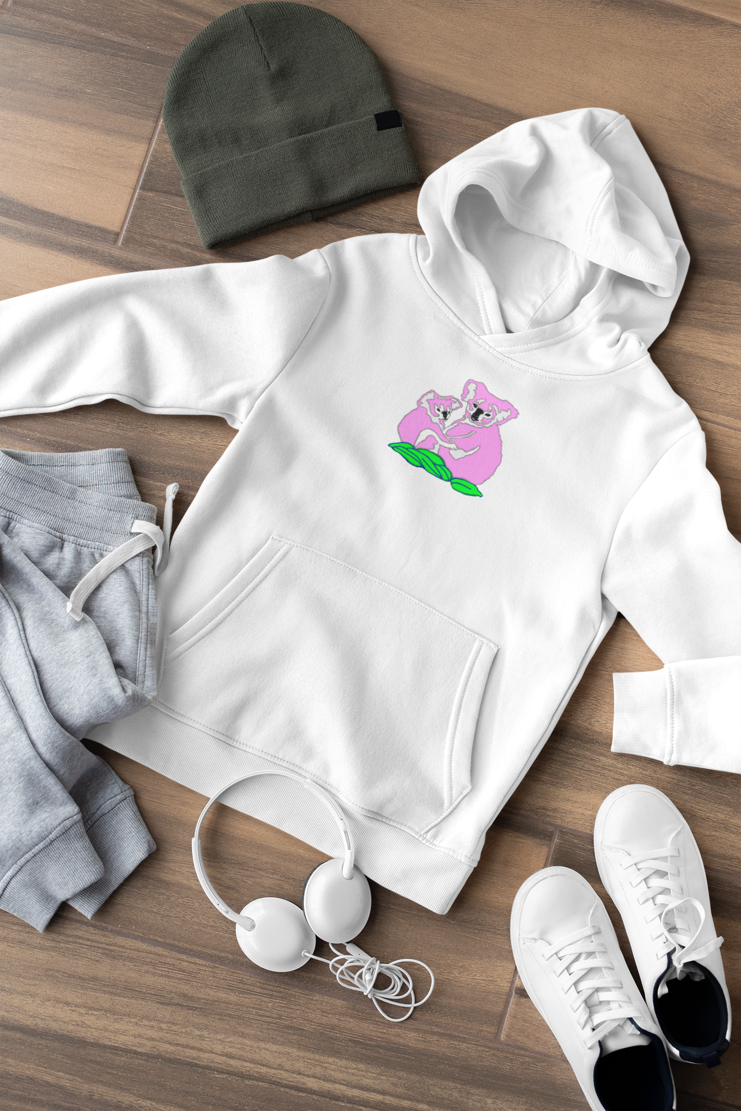 White hoodie with a graphic design, gray beanie, gray sweatpants, white sneakers, and earbuds on a wooden surface.