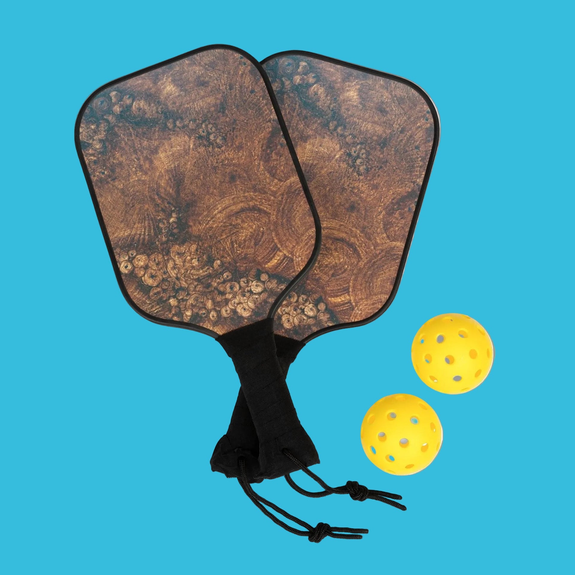 Two wooden pickleball paddles designed in Burlwood with a black drawstring bag and three yellow pickleballs 