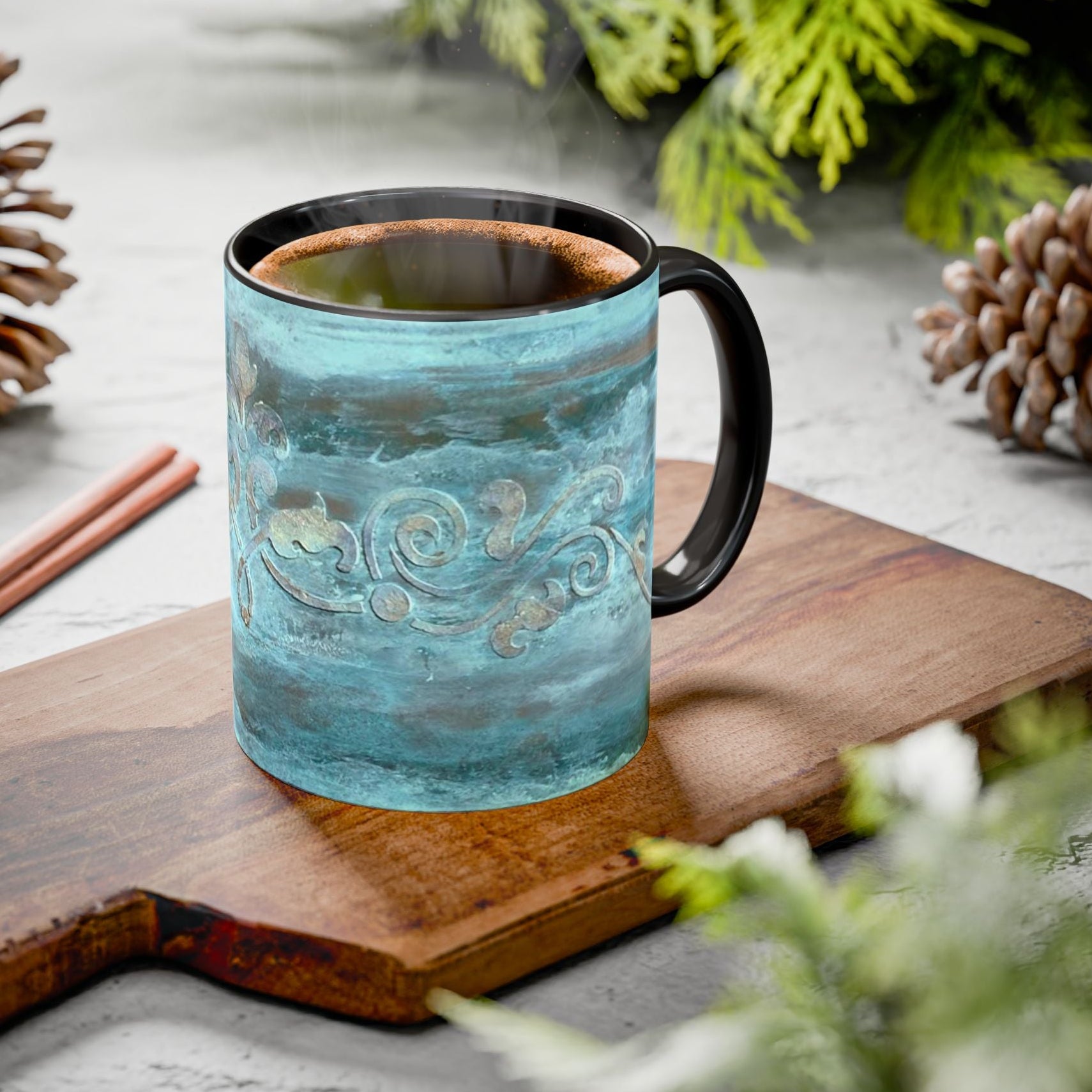 Teal mug with black handle on a wooden cutting board with decorative scroll elements