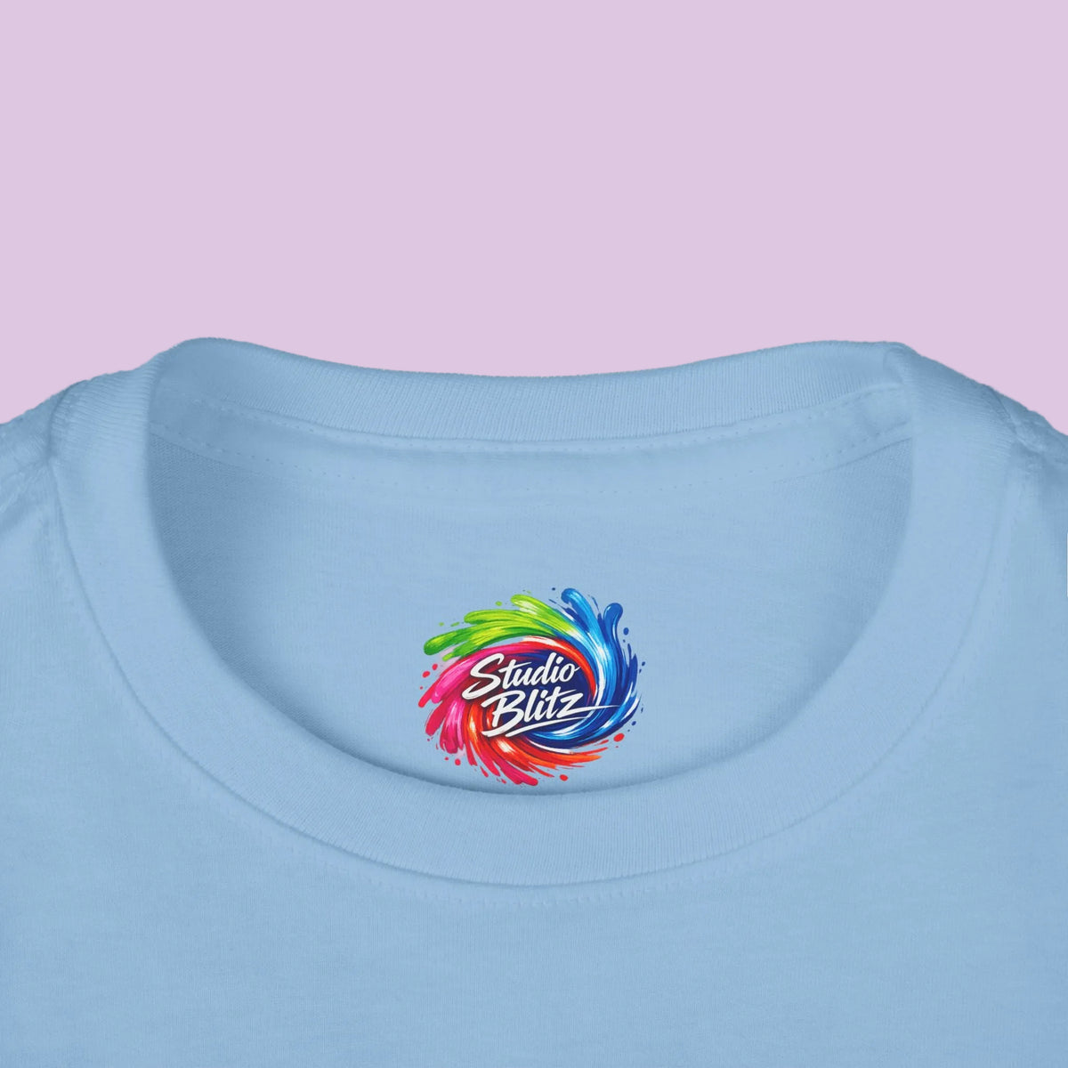 Close-up of a light blue crewneck t-shirt featuring a colorful 'Studio Blitz' circular logo printed on the inside of the collar.