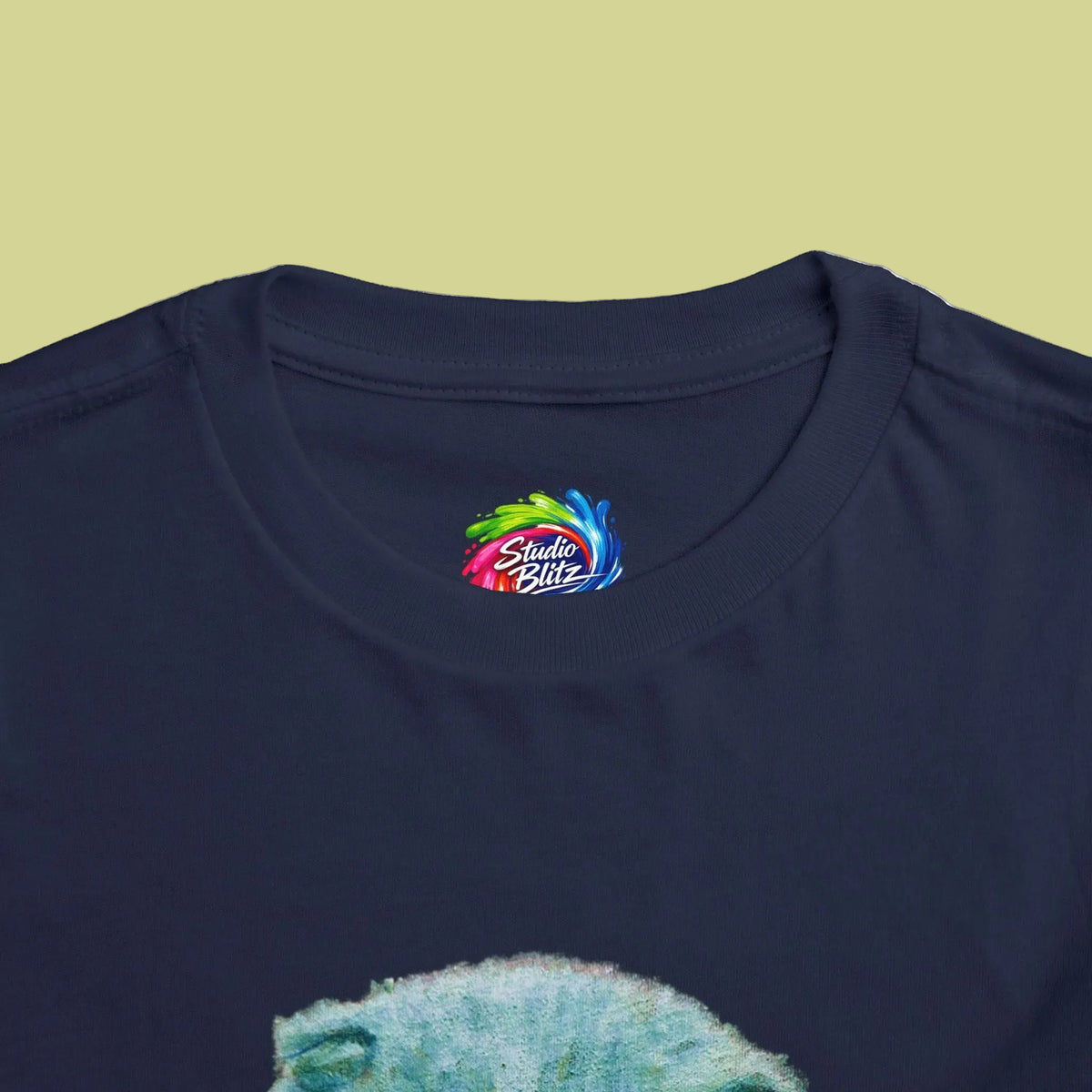 Close-up of a navy blue t-shirt collar featuring a colorful 'Studio Blitz' logo printed inside the neck, with a textured green graphic partially visible at the bottom.