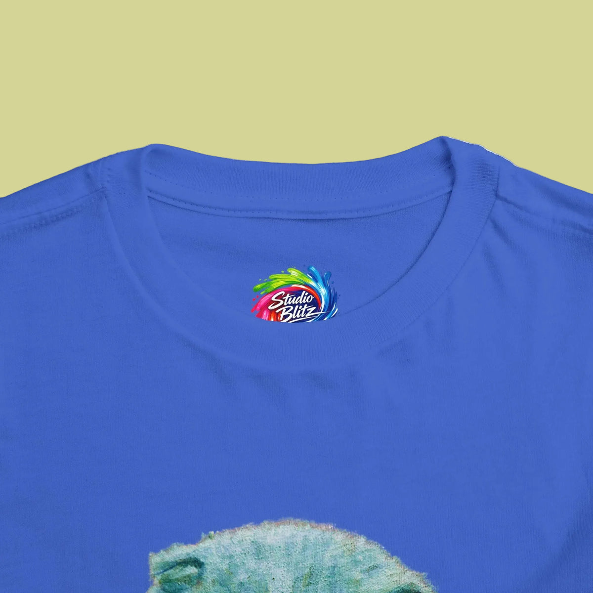 Close-up of a royal blue t-shirt  crew neck showing the inner neck label with a colorful 'Studio Blitz' logo and the top of a green textured graphic print below.